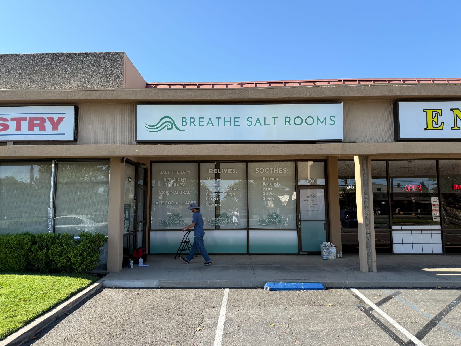 Breathe Salt Rooms storefront: a white fascia sign with a green wave logo above windows filled with cut and printed vinyl listing services and benefits, plus a wave motif along the glass
