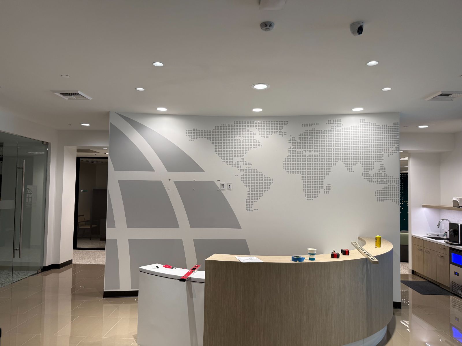 Curved reception wall behind a front desk with a large gray graphic: a dotted world map and sweeping globe grid lines applied in printed and cut vinyl to the interior wall