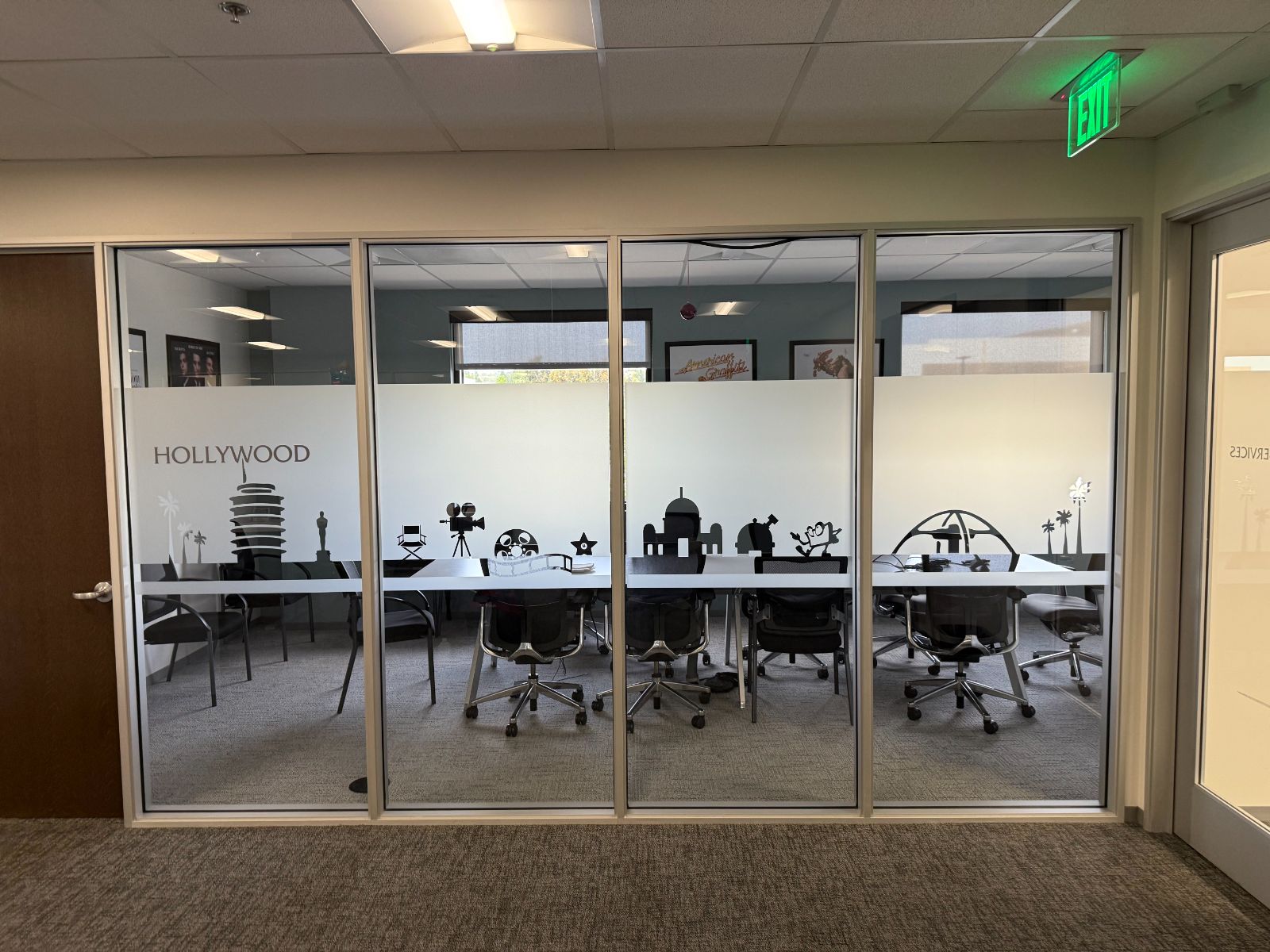 Glass-walled conference room with a frosted privacy band across the lower glass, decorated with a black Hollywood-themed skyline of film icons and the word HOLLYWOOD