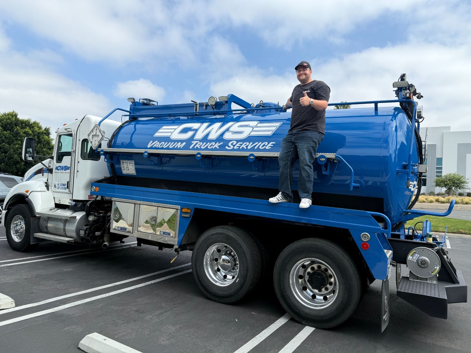 Blue CWS vacuum tanker truck in a parking lot with a man standing on the deck giving a thumbs up: large white 'CWS Vacuum Truck Service' vinyl graphics along the tank