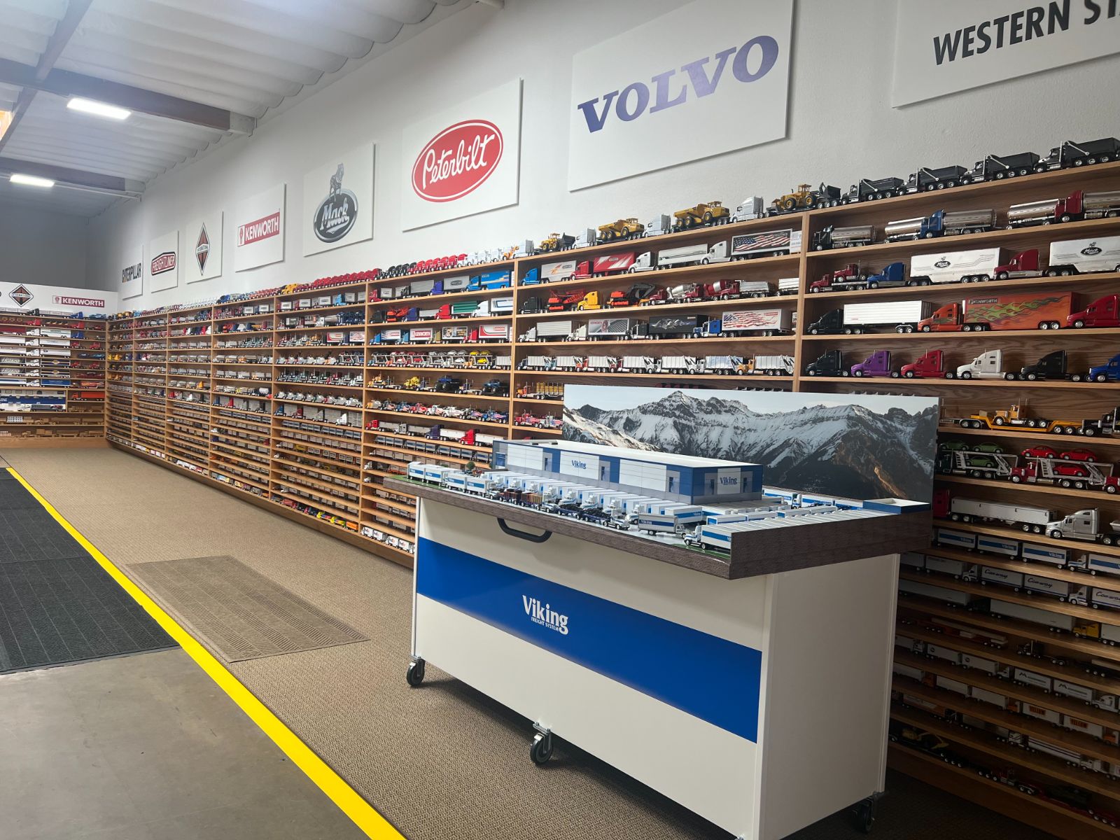 Interior of the Hi Sign sign shop in Brea: rows of shelving stocked with reference models and materials along a wall, with a mobile work cart in the aisle