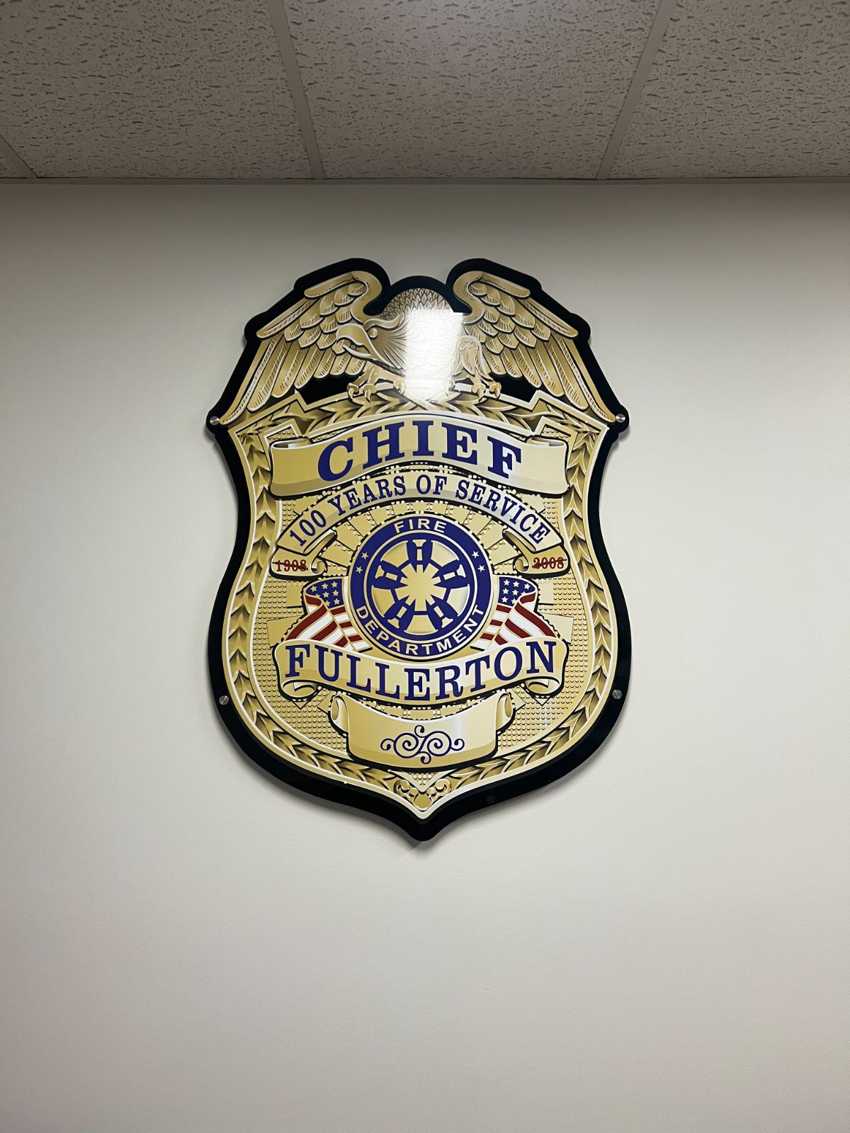Large badge-shaped wall plaque reading 'Chief · Fullerton · Fire Department · 100 Years of Service': a full-color fire chief badge printed on clear acrylic and standoff-mounted on an interior wall