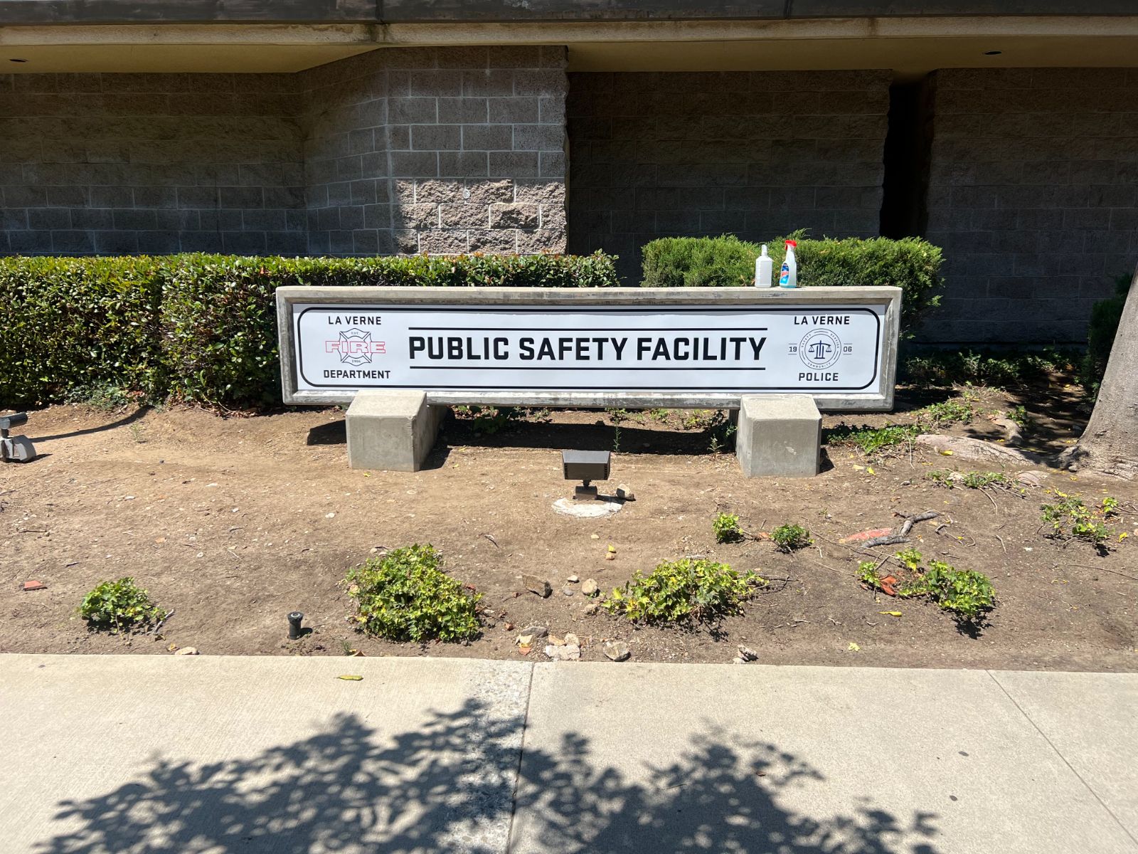 Low monument sign reading 'Public Safety Facility' set into a concrete base outside a masonry building: black text with a La Verne Fire Department crest on the left and a La Verne Police seal on the right