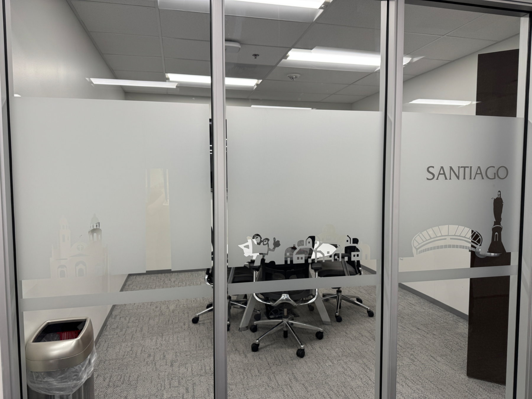 Glass office wall with a frosted privacy band carrying a cut-vinyl skyline and the room name SANTIAGO