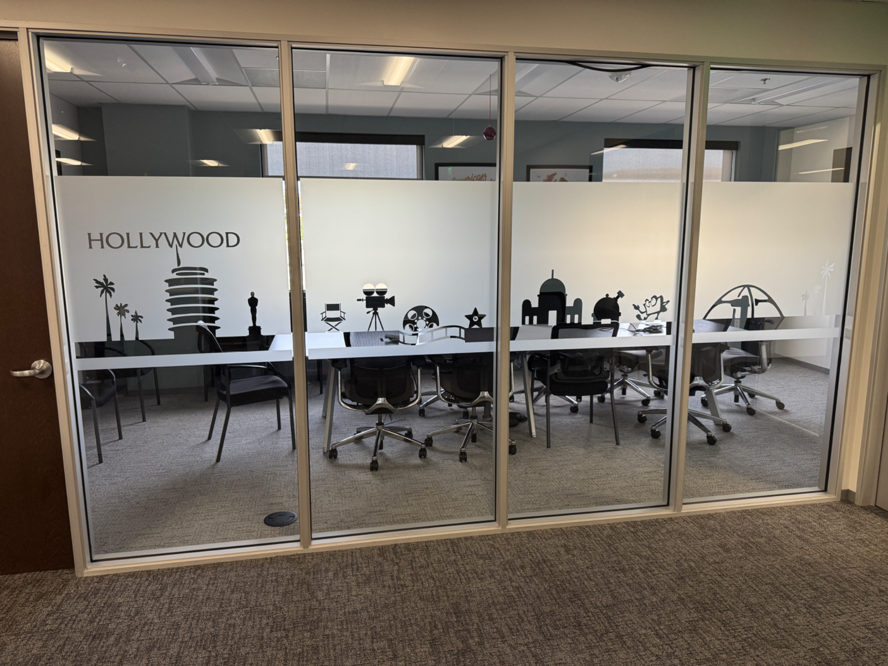 Glass meeting room wall with a frosted band carrying a cut-vinyl Hollywood skyline and the room name HOLLYWOOD