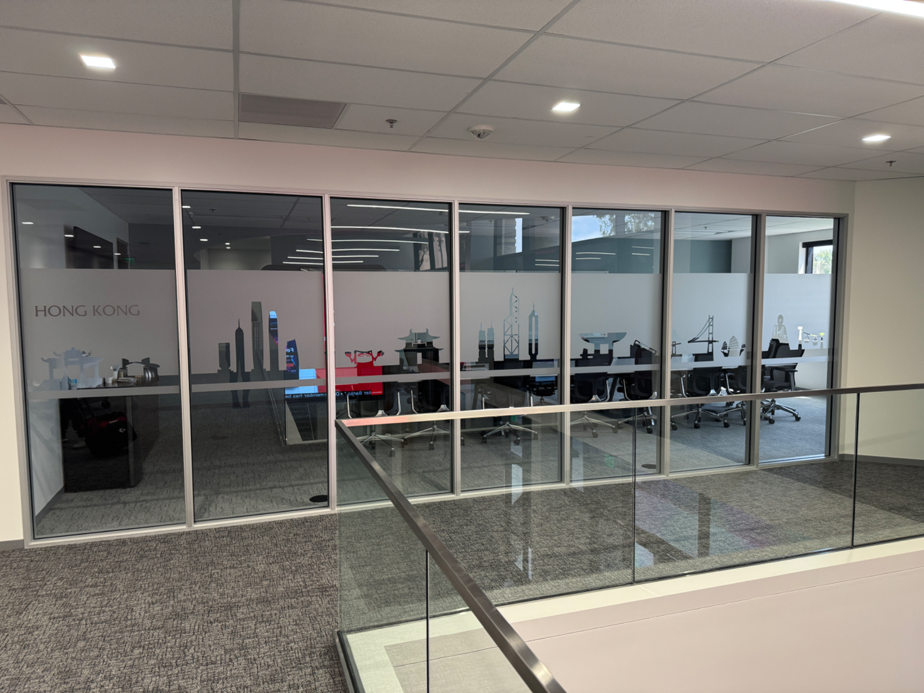 Glass-walled meeting room on an office mezzanine with a frosted privacy band carrying a cut-vinyl Hong Kong skyline and the room name HONG KONG