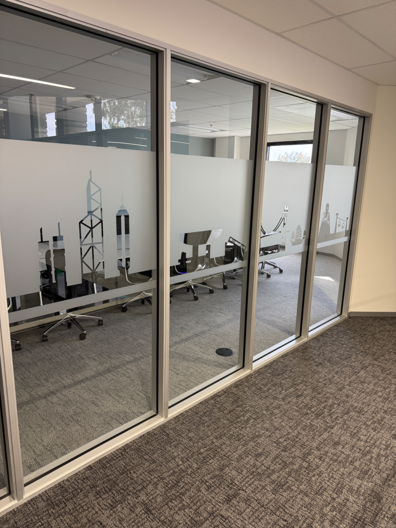 Long run of glass office wall with a continuous frosted privacy band carrying cut-vinyl city skyline graphics