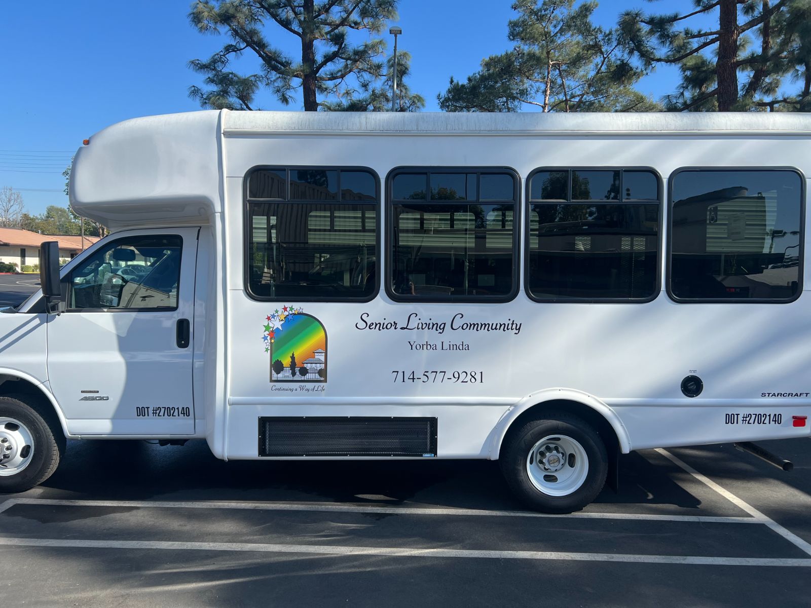 Driver-side vehicle graphics on a white Starcraft shuttle bus for Senior Living Community Yorba Linda: printed vinyl logo and die-cut lettering with business name, city, and phone number on the exterior body panel