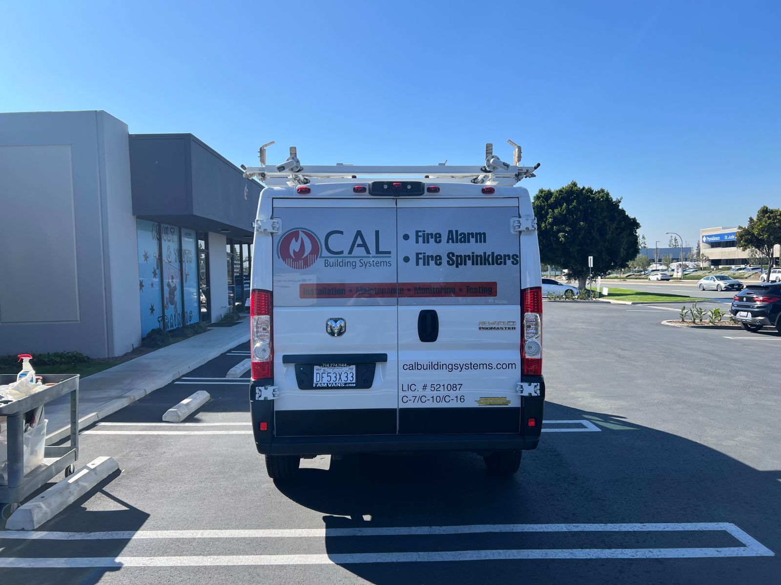 Rear of a white Ram ProMaster service van with printed vinyl graphics for CAL Building Systems: flame logo, company name, and a Fire Alarm / Fire Sprinklers service list