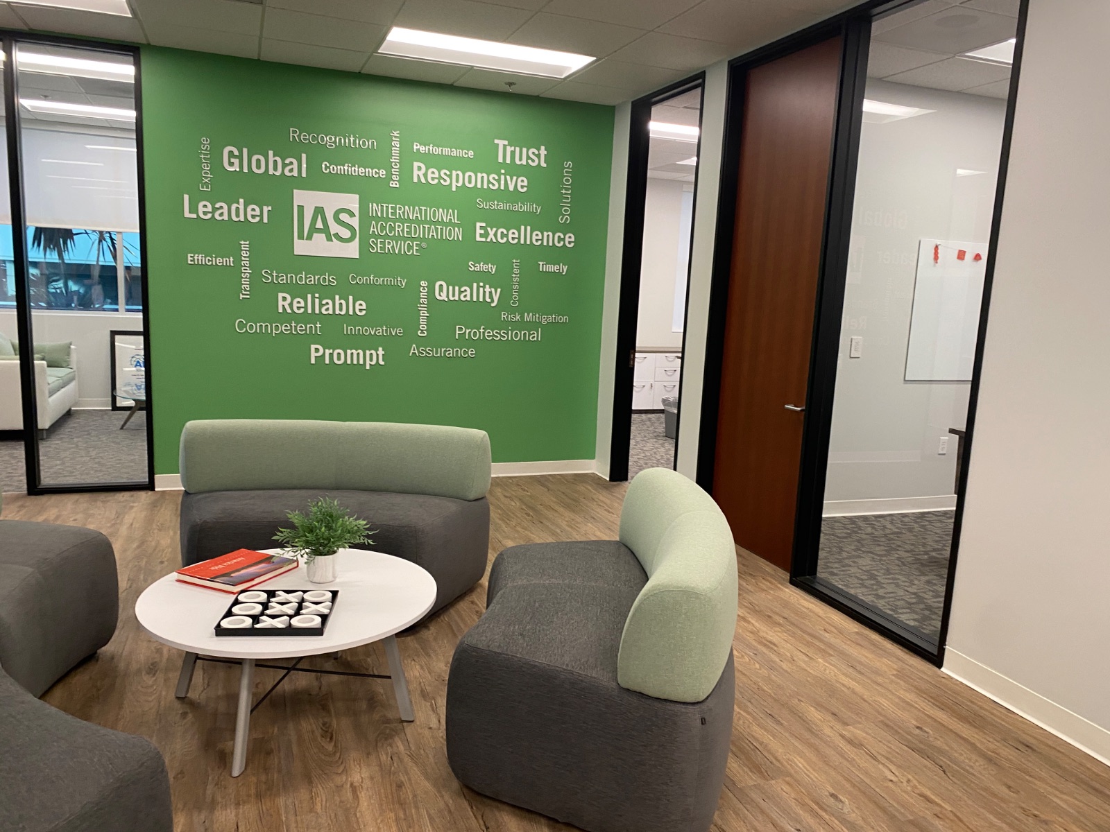 Office lounge with grey and green soft seating in front of the green cut-vinyl word-cloud wall