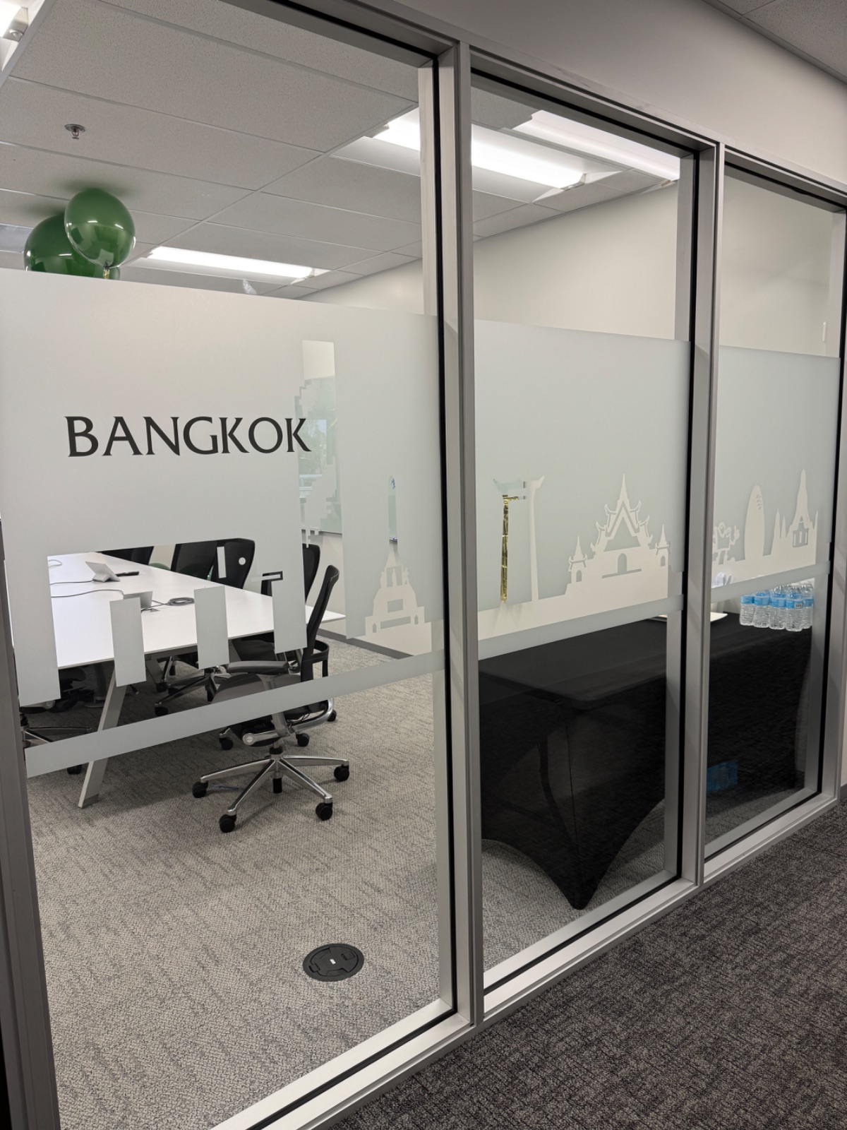 Glass-walled office room with a frosted band carrying a cut-vinyl Bangkok skyline and the room name BANGKOK