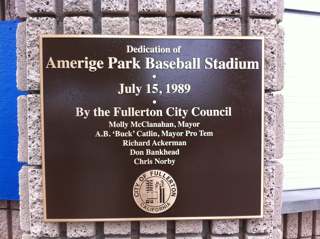 Bronze-tone dedication plaque with raised cream lettering reading 'Dedication of Amerige Park Baseball Stadium, July 15, 1989, By the Fullerton City Council' with council member names and the City of Fullerton seal, mounted on a split-face block wall