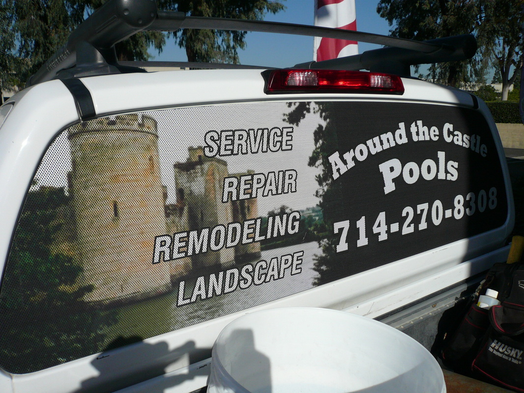 Rear window of a white pickup truck covered with a see-through perforated vinyl graphic for Around the Castle Pools listing service, repair, remodeling, and landscape with a phone number